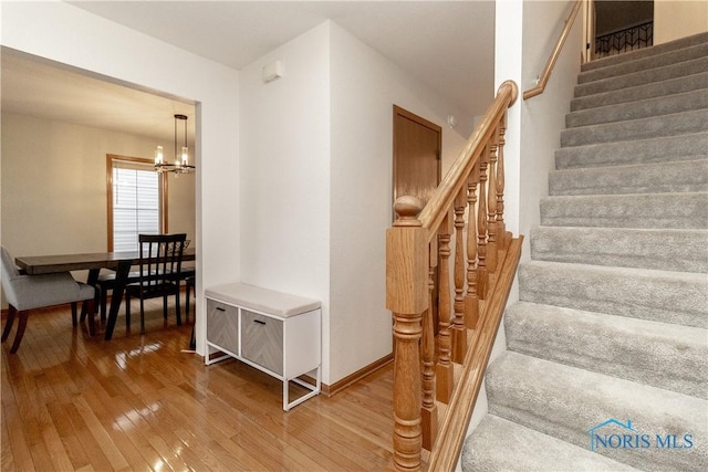stairs featuring hardwood / wood-style flooring, baseboards, and a chandelier
