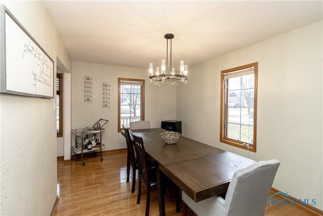 dining space with light wood-type flooring, baseboards, and an inviting chandelier