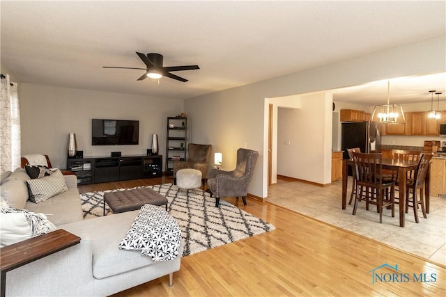 living area featuring ceiling fan with notable chandelier, light wood-type flooring, and baseboards