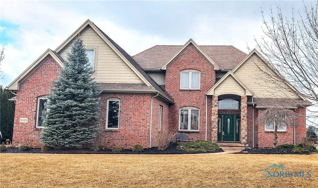 traditional home with a front yard, brick siding, and roof with shingles