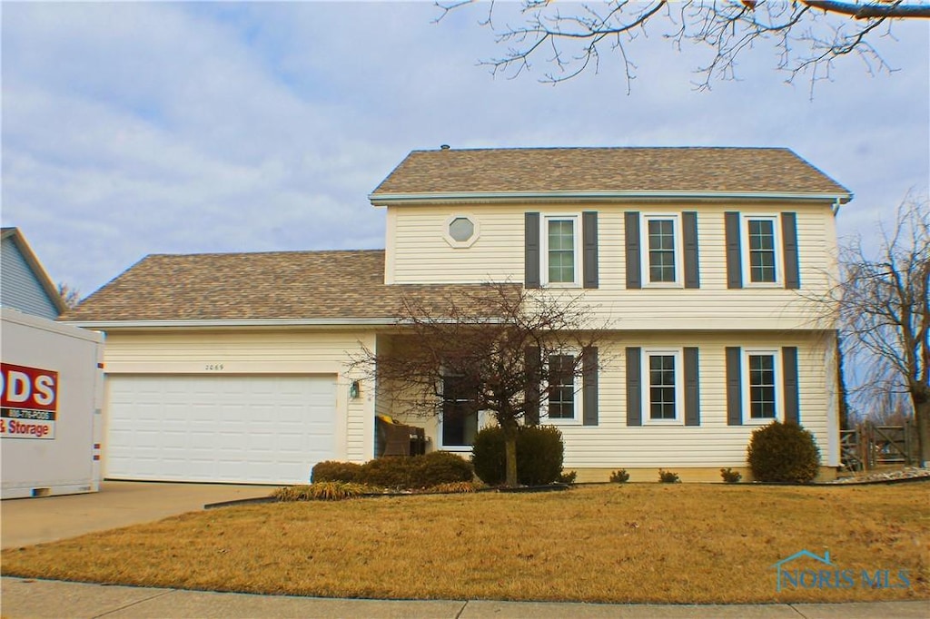 colonial inspired home with a front lawn, concrete driveway, a shingled roof, and an attached garage