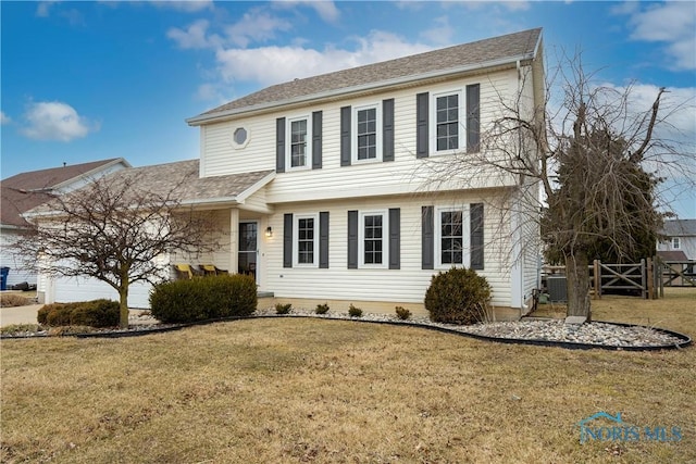 colonial house featuring an attached garage, a shingled roof, a front yard, and fence