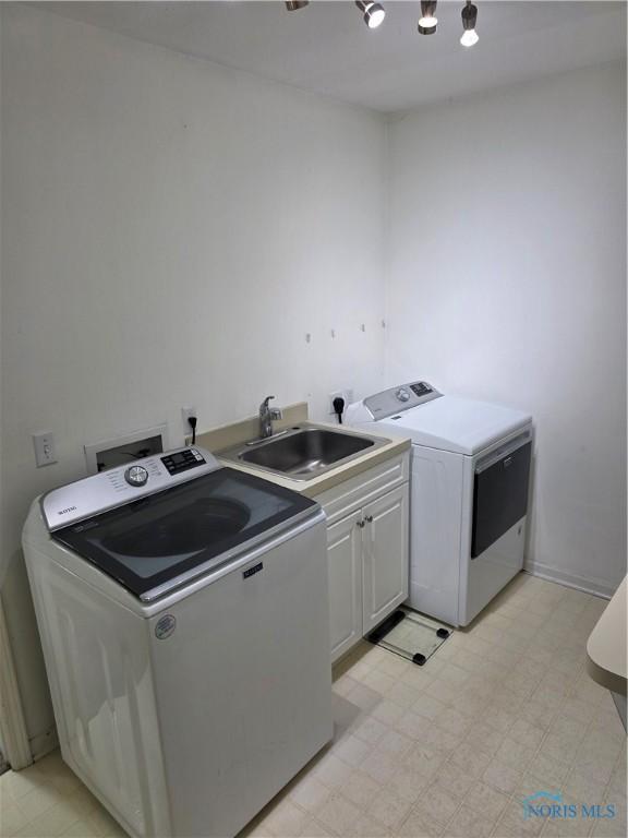 clothes washing area with light floors, cabinet space, washer and clothes dryer, and a sink