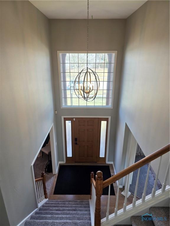 foyer entrance featuring a towering ceiling, stairs, baseboards, and a notable chandelier