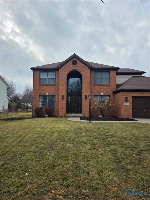 traditional home featuring an attached garage, driveway, brick siding, and a front yard