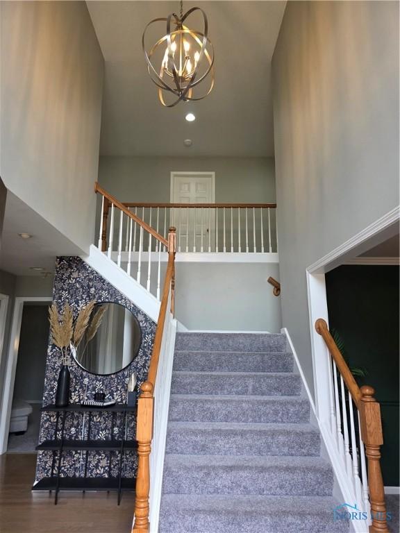 stairway featuring a high ceiling, an inviting chandelier, and wood finished floors