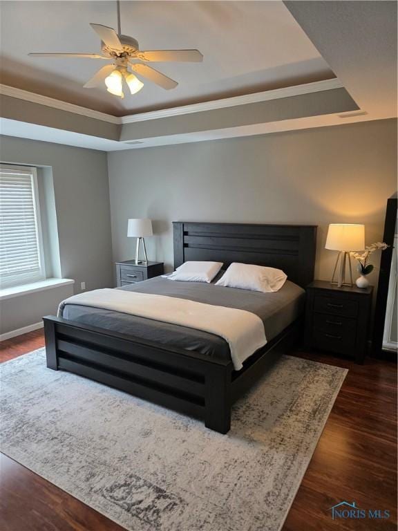 bedroom with ornamental molding, a raised ceiling, ceiling fan, and dark wood-style flooring