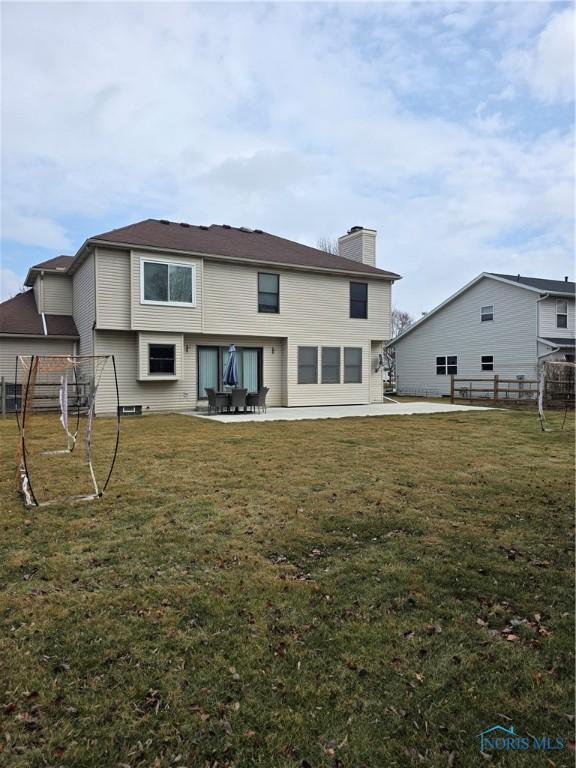 rear view of property featuring a chimney, a lawn, a patio area, and fence