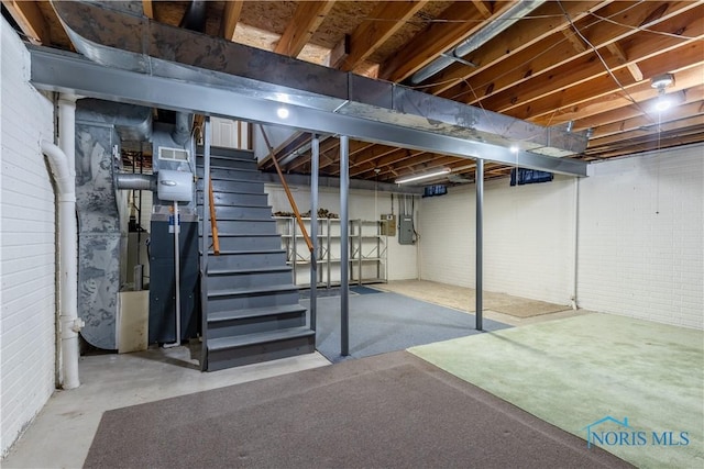 unfinished basement with stairs, brick wall, visible vents, and electric panel