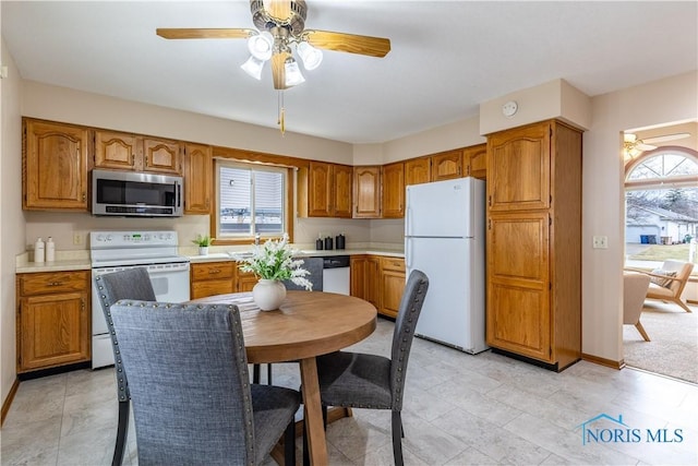 kitchen with white appliances, a ceiling fan, baseboards, light countertops, and brown cabinetry