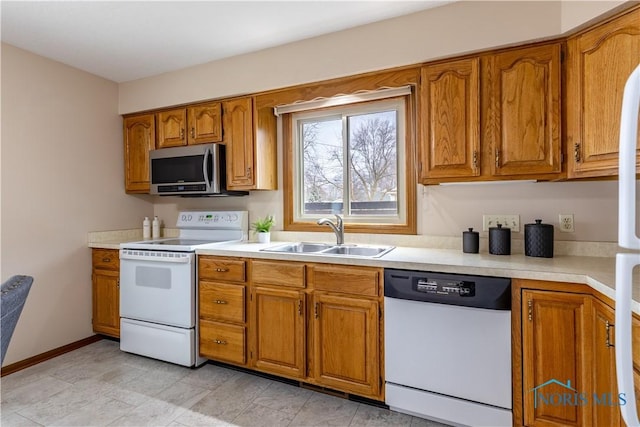 kitchen with white appliances, baseboards, brown cabinetry, light countertops, and a sink