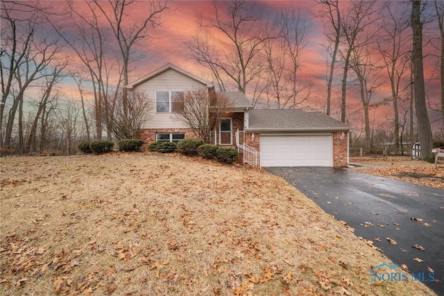 split level home with an attached garage, aphalt driveway, and brick siding