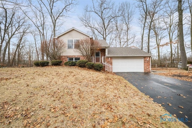 split level home featuring a garage, brick siding, and aphalt driveway