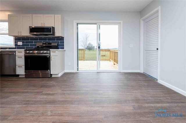 kitchen featuring baseboards, appliances with stainless steel finishes, decorative backsplash, and dark wood finished floors