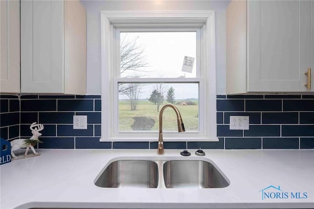 kitchen with white cabinets, backsplash, light countertops, and a sink