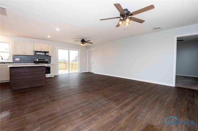 kitchen featuring decorative backsplash, gas range, open floor plan, dark wood-type flooring, and light countertops