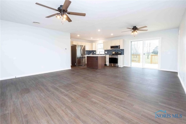 kitchen with stainless steel appliances, a kitchen island, open floor plan, light countertops, and backsplash