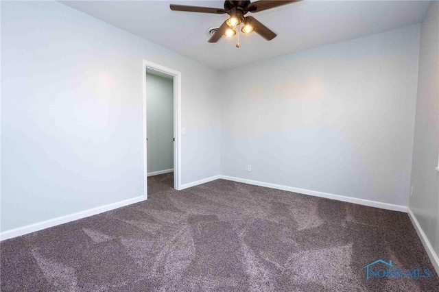 empty room with baseboards, dark carpet, and ceiling fan