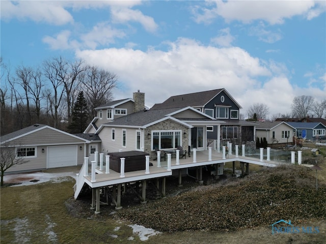 back of property with a garage, stone siding, a chimney, and a wooden deck