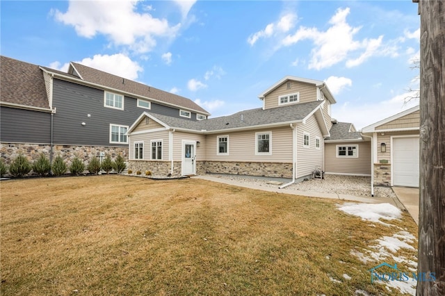 back of house with a shingled roof, stone siding, a yard, and an attached garage