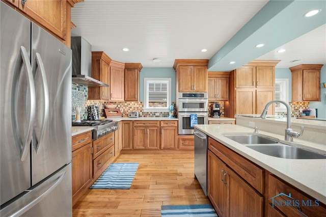 kitchen featuring light wood finished floors, light countertops, stainless steel appliances, wall chimney range hood, and a sink