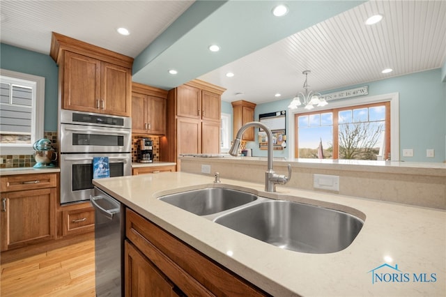 kitchen featuring light stone counters, brown cabinets, stainless steel appliances, pendant lighting, and a sink