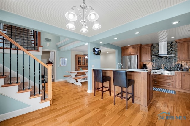 kitchen with a breakfast bar area, visible vents, wall chimney range hood, appliances with stainless steel finishes, and decorative backsplash