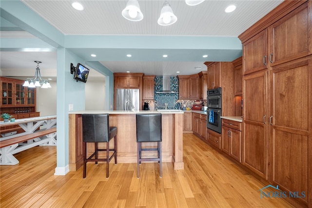 kitchen with brown cabinets, wall chimney exhaust hood, decorative backsplash, freestanding refrigerator, and a kitchen breakfast bar