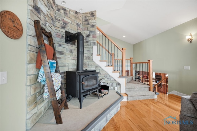 living room with stairs, wood finished floors, a wood stove, and baseboards