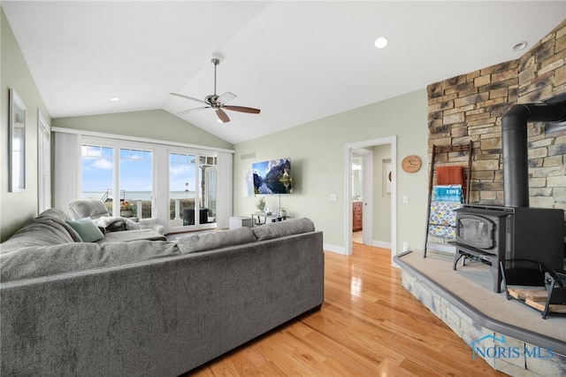 living room with light wood finished floors, baseboards, a ceiling fan, lofted ceiling, and a wood stove