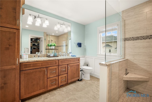 bathroom featuring double vanity, a wainscoted wall, walk in shower, and a sink