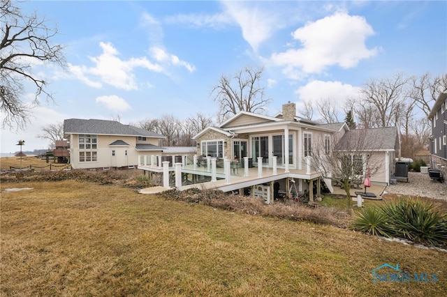 rear view of house with a chimney, cooling unit, a lawn, and a wooden deck