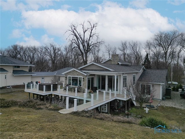 rear view of house featuring a shingled roof, a lawn, a chimney, and a wooden deck