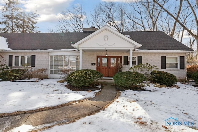 view of front of home featuring brick siding, a chimney, and a shingled roof