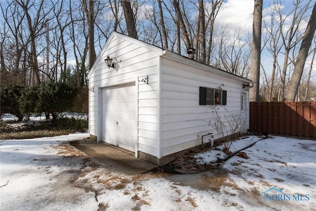 snow covered garage featuring a garage and fence