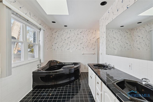 bathroom with wallpapered walls, a skylight, a sink, tile patterned flooring, and tile walls