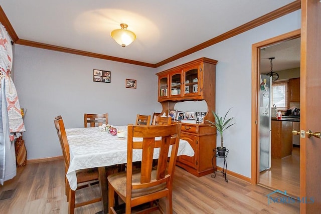 dining space with crown molding, light wood-style flooring, and baseboards