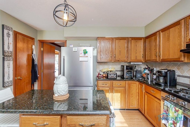 kitchen featuring dark stone counters, stainless steel appliances, backsplash, and brown cabinets