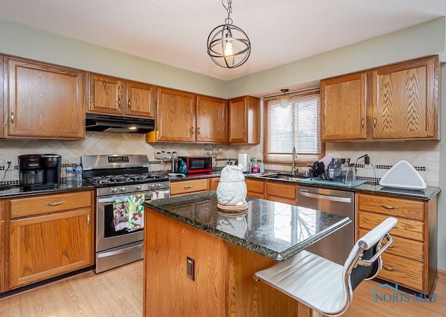 kitchen with under cabinet range hood, stainless steel appliances, a sink, light wood-type flooring, and brown cabinets