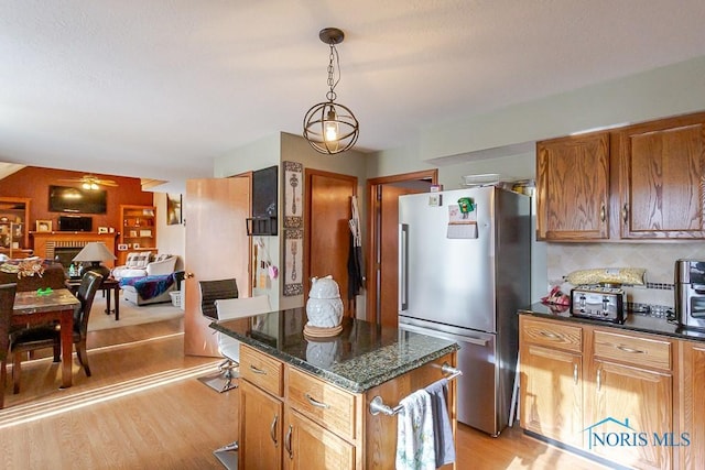 kitchen featuring a fireplace, backsplash, freestanding refrigerator, open floor plan, and light wood-type flooring