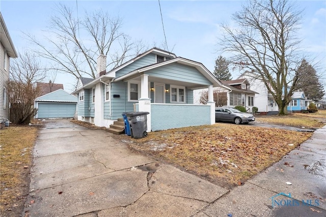 bungalow-style home featuring an outbuilding, a porch, a chimney, and a detached garage