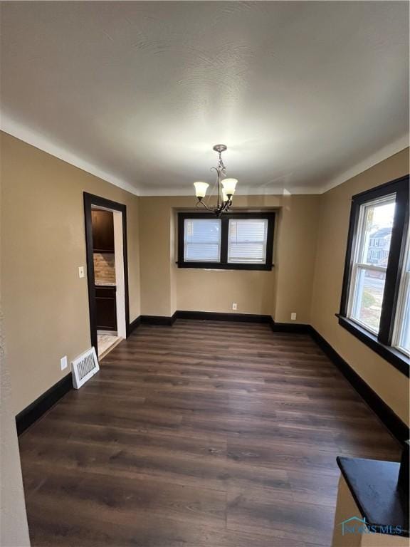 spare room featuring an inviting chandelier, dark wood-style flooring, baseboards, and visible vents
