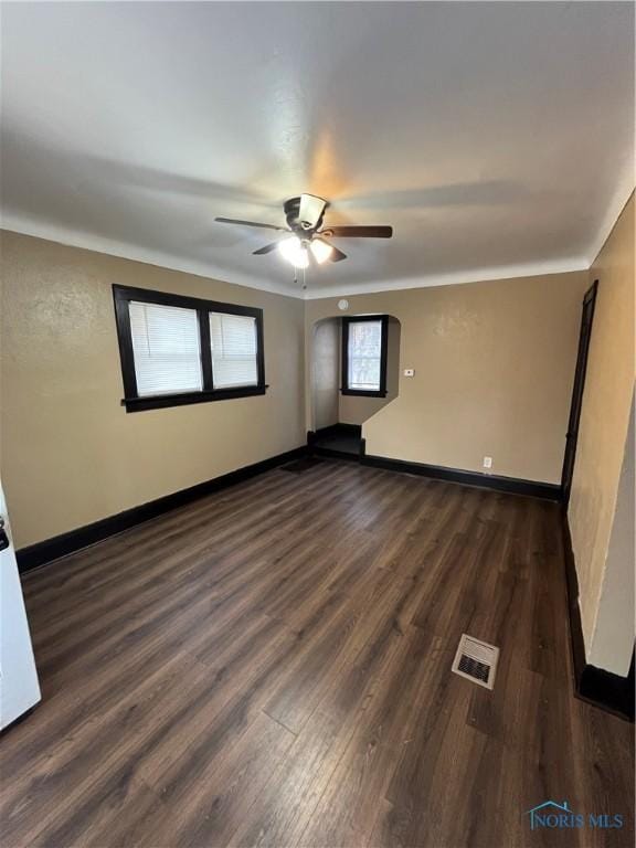 empty room with dark wood-type flooring, baseboards, ceiling fan, and visible vents