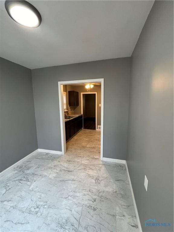 empty room with marble finish floor, baseboards, and a sink