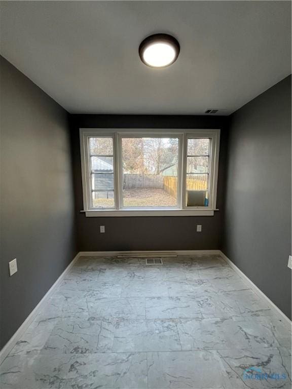 spare room featuring baseboards, marble finish floor, and plenty of natural light