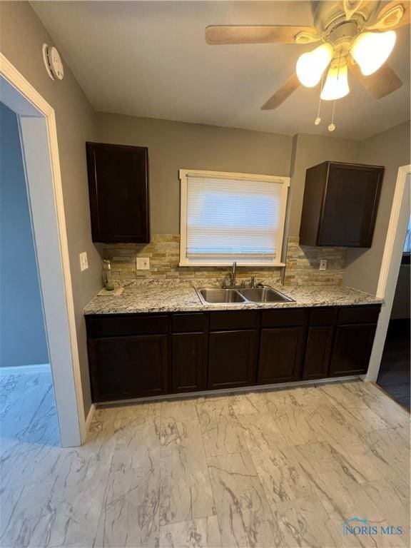 kitchen with backsplash, a sink, light stone countertops, marble finish floor, and dark brown cabinets