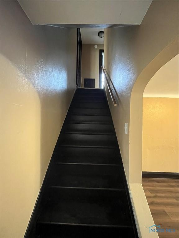 stairs featuring wood finished floors and arched walkways