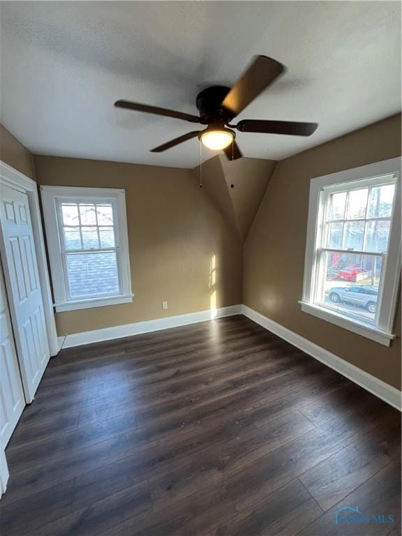 unfurnished bedroom featuring multiple windows, baseboards, and dark wood-type flooring