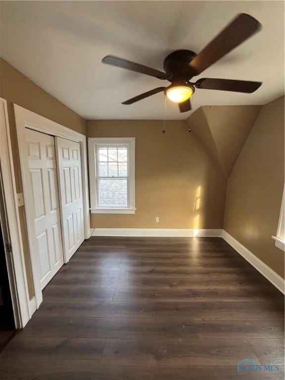 unfurnished bedroom featuring vaulted ceiling, a closet, dark wood finished floors, baseboards, and ceiling fan