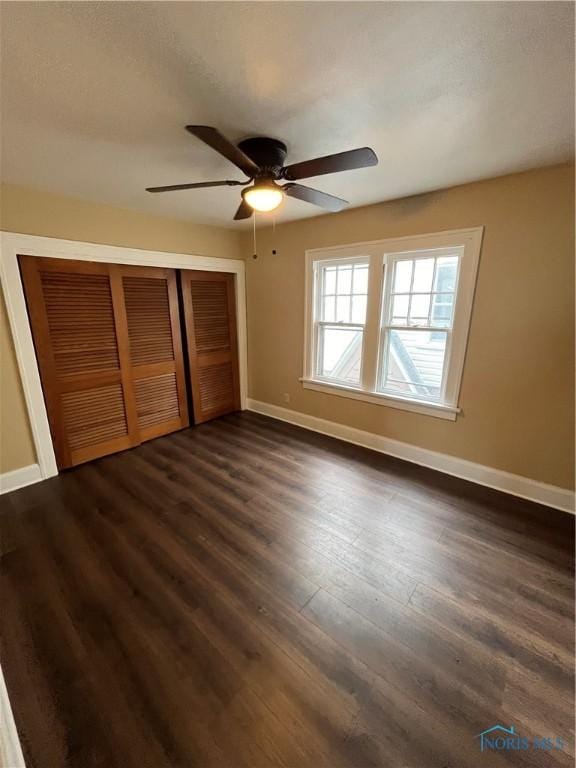 unfurnished bedroom with a closet, baseboards, ceiling fan, and dark wood finished floors